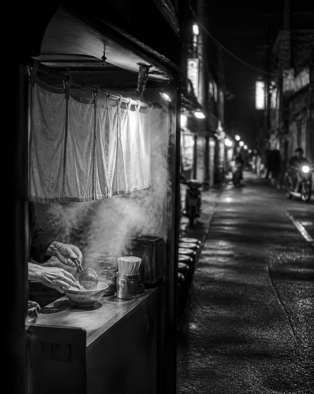 夜の路地に立つ小さなラーメン店で調理する店主の手元